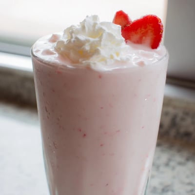 Thick strawberry milkshake in a tall glass with a swirl of whipped topping